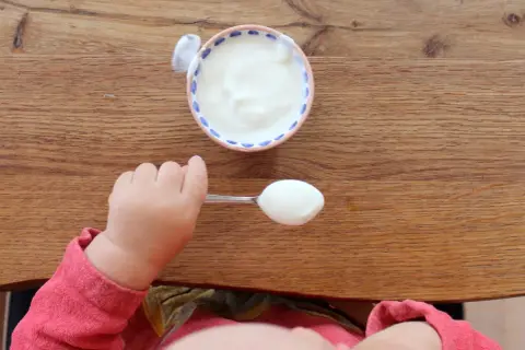 Kleiner Löffel mit Joghurt für ein Baby. Wann ist Joghurt für Babys geeignet?