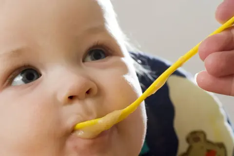 Ein Baby wird mit einem gelben Löffel gefüttert. Der Brei ist warm, perfekt zum babybrei warm halten.