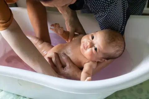 Ein Baby wird in einer Babybadewanne gebadet. Die Eltern prüfen die **Badetemperatur Baby**, damit es sich wohlfühlt.