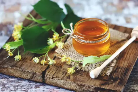 Ein Glas Honig mit Lindenblüten und einem Honiglöffel. Perfekt zum Honig essen beim Stillen für süße Momente.