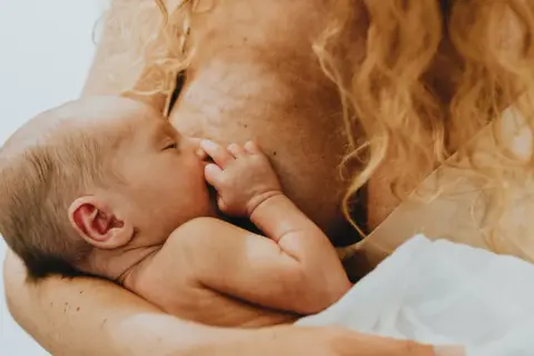 Ein Baby schreit beim Stillen, die Mutter hält es liebevoll.