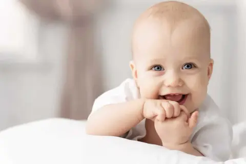 Ein lächelndes Baby mit blauen Augen, das auf einem weißen Kissen liegt. Tolle 4. sprung baby erfahrungen!