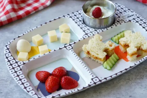 Leckeres Essen für ein Kleinkind (2 Jahre): Erdbeeren, Käsewürfel, ein Ei, Gurkenscheiben und ein süßes Sandwich.
