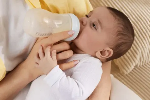Baby trinkt aus Flasche, vielleicht wegen Wachstumsschub. Es spuckt danach mehr, aber das ist normal.