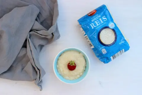 Ein Schälchen Milchreis mit Erdbeere, daneben eine Packung Milchreis. Perfekt für kleine Genießer.