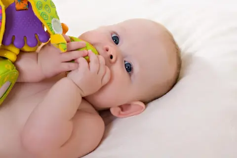 Baby mit blauen Augen erkundet sein buntes Spielzeug. Ein typischer Moment im 19 wochen schub, voller Entdeckungen.