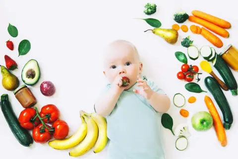 Baby mit Erdbeere im Mund, umgeben von Obst und Gemüse, das für die Lebensmittel und Milchbildung wichtig ist.