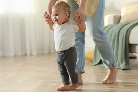 Ein Baby lernt laufen, gehalten von einer Person. Die ersten Schritte sind aufregend, wann stehen Babys?
