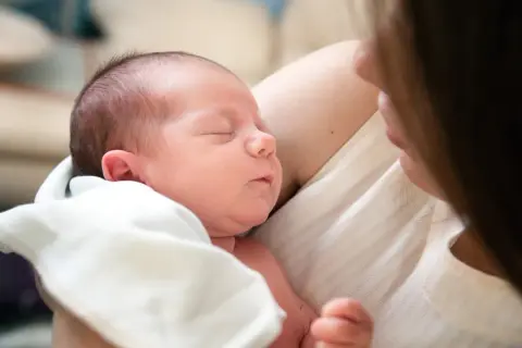 Ein Neugeborenes schläft friedlich in den Armen seiner Mutter. Die Nähe und Wärme zeigen die vielen Vorteile stillen.