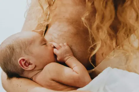 Ein Baby trinkt an der Brust, sein Kalorienbedarf wird auf natürliche Weise gestillt. Die Mutter hält es liebevoll.