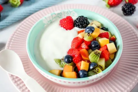 Ein Schüsselchen Joghurt mit frischem Obstsalat, perfekt für ein Kleinkind. Erdbeeren, Blaubeeren, Kiwi und Pfirsichstücke machen den Joghurt zum Genuss.