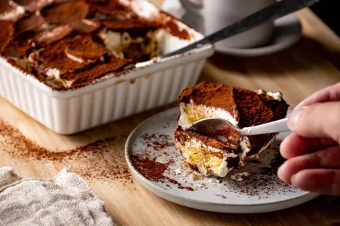 Ein Stück Tiramisu wird mit einer Gabel aus einer Auflaufform genommen. Perfekt für die Stillzeit!