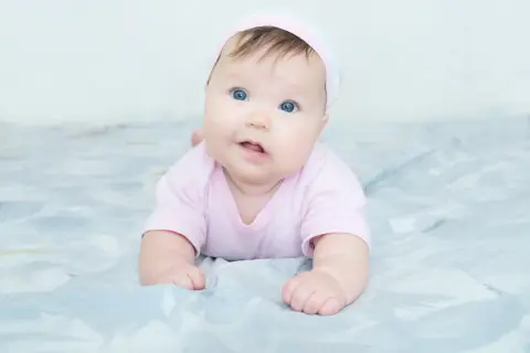 Blauäugiges Baby in rosa Strampler und Mütze. Mögliche kiss-syndrom symptome wie Kopfhaltung können hier nicht erkannt werden.