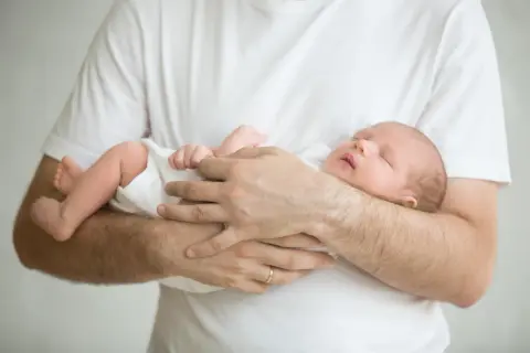 Ein Vater hält sein schlafendes Baby. Das Baby wedelt mit Armen und Beinen im Schlaf.