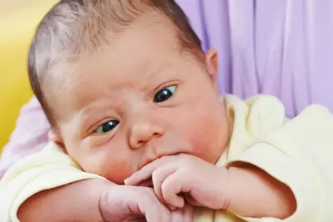 Ein süßes Baby mit schielenden Augen, das nachdenklich auf seinen Fingern kaut.