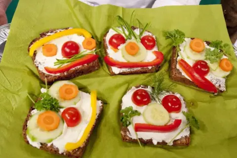 Lustige Gesichter auf belegten Broten: Fingerfood, das Kinder lieben. Bunte Gemüsesorten wie Paprika, Gurke und Karotte schmücken die Brotscheiben.
