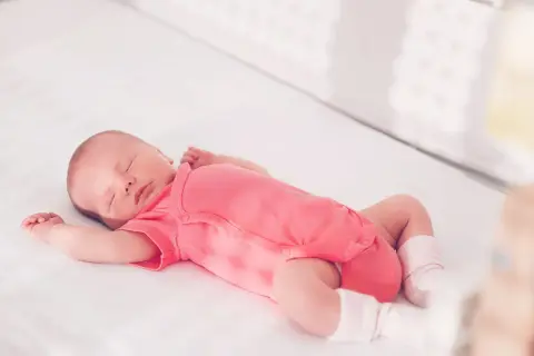 Ein schlafendes Baby in einem pinken Strampler streckt sich durch, während es in seinem Bettchen ruht.