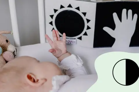 Ein Baby mit 2 Wochen erkundet mit seiner Hand ein Schwarz-Weiß-Buch mit Sonne und Hand.