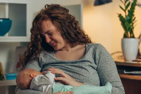 Mutter mit rissigen Brustwarzen stillt ihr Baby liebevoll, trotz des Schmerzes.