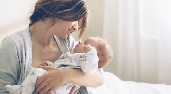 Mutter hält ihr Neugeborenes liebevoll im Arm. Ein Moment purer Zuneigung, eine stille Empfehlung für die innige Bindung zwischen Mutter und Kind.