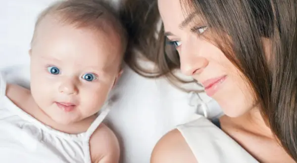 Ein Baby von 23 Wochen mit strahlend blauen Augen blickt neugierig in die Kamera, während seine Mutter es liebevoll ansieht.