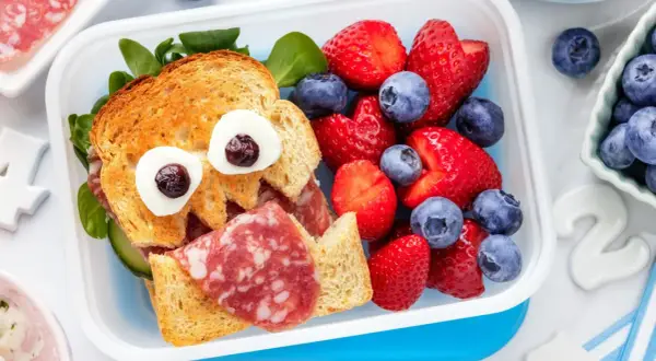 Ein lustiges Vesper-Essen Kita: ein Toast-Gesicht mit Wurst, Gurke und Beeren.