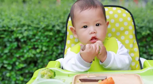 Ein süßes Baby isst im Hochstuhl. Der **Kalorienbedarf Baby 10 Monate** ist wichtig für seine Entwicklung.