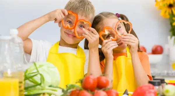 Zwei Kinder mit Paprikaringen vor den Augen, die Spaß beim Kochen haben. Gesunde Ernährung ist wichtig für den **Kalorienbedarf Kleinkind**.