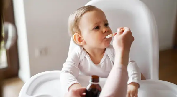 Ein Baby im Hochstuhl erhält Medikamente per Löffel. Die Eltern wechseln zwischen Ibuprofen und Paracetamol alle 4 Stunden, um Fieber zu senken.