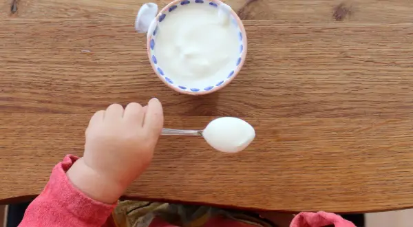 Kleiner Löffel mit Joghurt für ein Baby. Wann ist Joghurt für Babys geeignet?