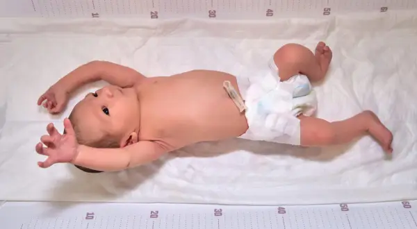 Neugeborenes Baby mit ausgestreckten Armen und Beinen, das den Suchreflex zeigt. Die Messskala am Rand deutet auf eine Größenmessung hin.