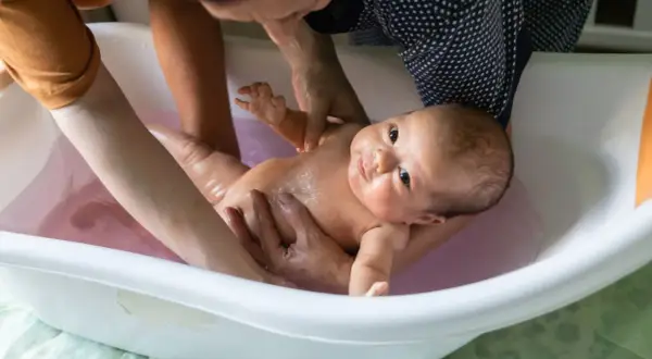 Ein Baby wird in einer Babybadewanne gebadet. Die Eltern prüfen die **Badetemperatur Baby**, damit es sich wohlfühlt.