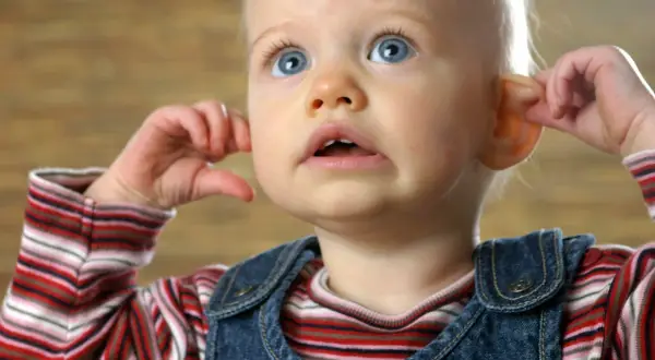 Kleines Baby kratzt sich am Ohr, die Augen weit aufgerissen.