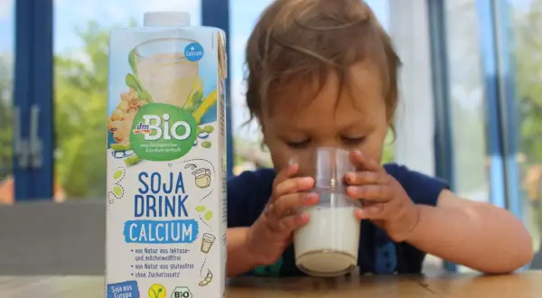 Ein süßes Kleinkind trinkt Soja Drink Calcium. Die Packung steht daneben.
