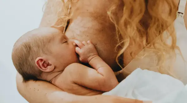 Ein Baby schreit beim Stillen, die Mutter hält es liebevoll.