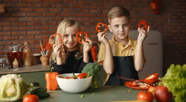Zwei Kinder halten Paprikaringe hoch. Sie lernen, was muss man essen um zu wachsen: viel Gemüse!