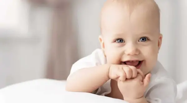 Ein lächelndes Baby mit blauen Augen, das auf einem weißen Kissen liegt. Tolle 4. sprung baby erfahrungen!