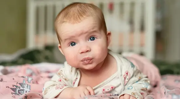 Baby mit blauen Augen liegt auf dem Bauch, sabbert und übt den 4 monats schub.