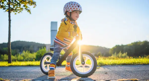 Kleiner Junge mit Helm auf Laufrad, strahlend im Sonnenuntergang. Ein echter Entwicklungsschub mit 3 Jahren!