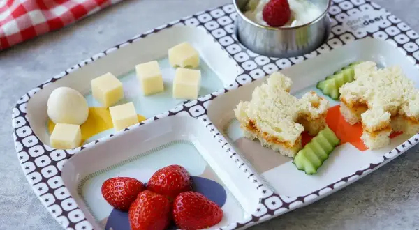 Leckeres Essen für ein Kleinkind (2 Jahre): Erdbeeren, Käsewürfel, ein Ei, Gurkenscheiben und ein süßes Sandwich.
