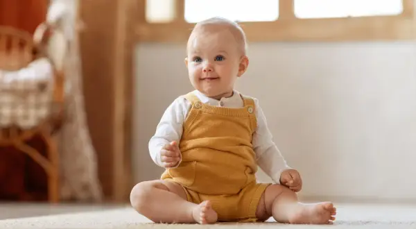 Ein fröhliches Baby sitzt auf dem Teppich. Die meisten Babys können ab dem 6. Monat sitzen.