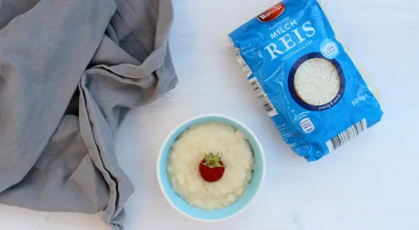 Ein Schälchen Milchreis mit Erdbeere, daneben eine Packung Milchreis. Perfekt für kleine Genießer.