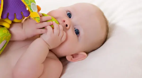 Baby mit blauen Augen erkundet sein buntes Spielzeug. Ein typischer Moment im 19 wochen schub, voller Entdeckungen.