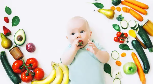 Baby mit Erdbeere im Mund, umgeben von Obst und Gemüse, das für die Lebensmittel und Milchbildung wichtig ist.