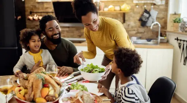 Familie am Esstisch, die ein Festessen genießt. Die Mutter reicht dem Sohn Salat, der wie mein Kind isst nicht 10 Jahre, hoffentlich probiert er.