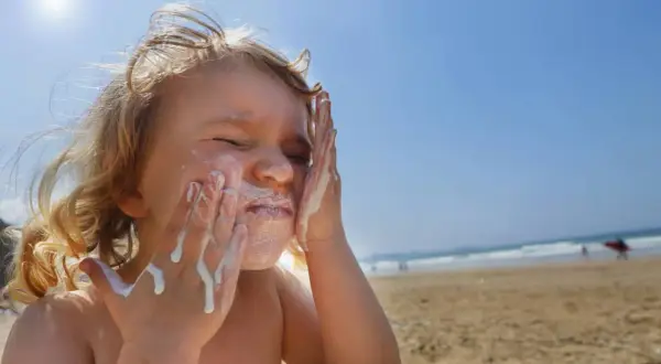 Kind schmiert sich Sonnencreme ins Gesicht. Bei Sonnenbrand helfen Hausmittel wie Quark oder Aloe Vera.