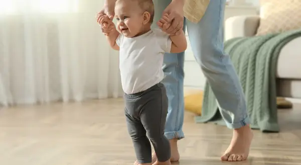 Ein Baby lernt laufen, gehalten von einer Person. Die ersten Schritte sind aufregend, wann stehen Babys?