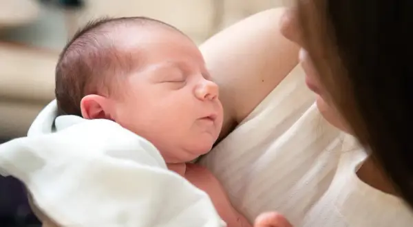 Ein Neugeborenes schläft friedlich in den Armen seiner Mutter. Die Nähe und Wärme zeigen die vielen Vorteile stillen.