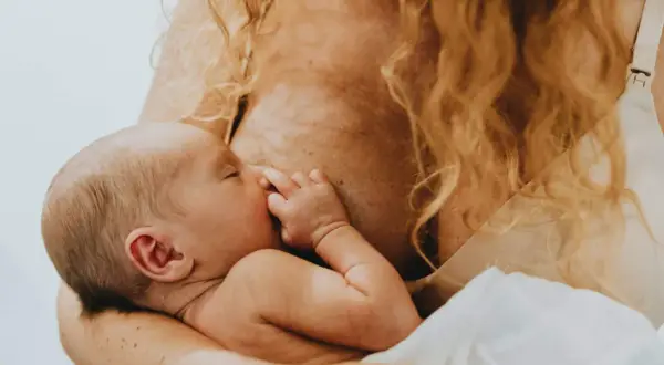 Ein Baby trinkt an der Brust, sein Kalorienbedarf wird auf natürliche Weise gestillt. Die Mutter hält es liebevoll.