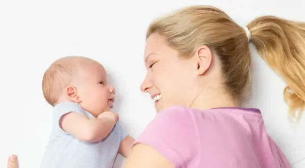 Ein lächelndes Baby, 2 Wochen alt, schaut seine Mutter an. Sie liegt neben ihm und lächelt zurück.